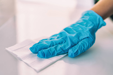 Hand wearing a blue latex glove wiping down a table top